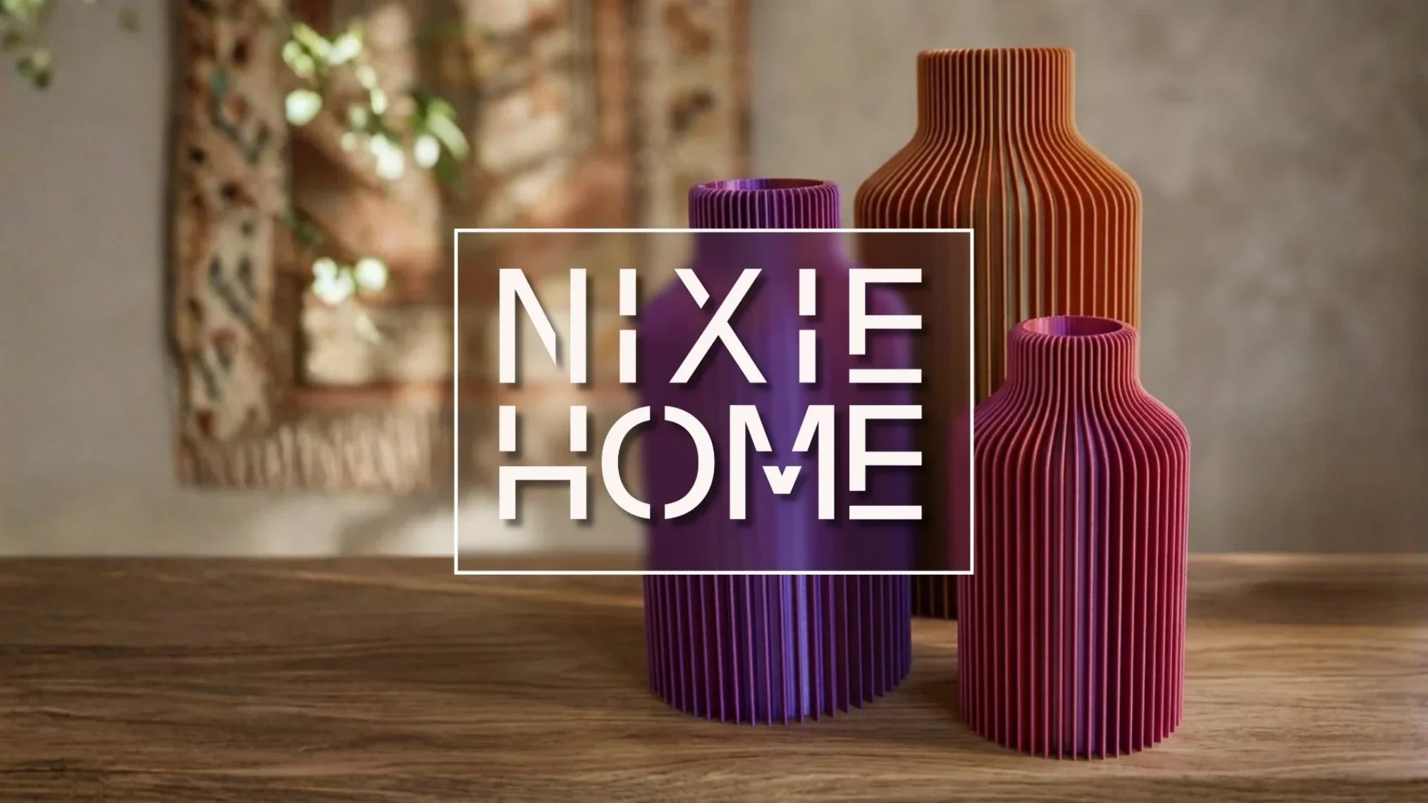 NIXE HOME - 3 Vasen hinter der Schrift auf einem Tisch. Farben sind pink, lila, orange.