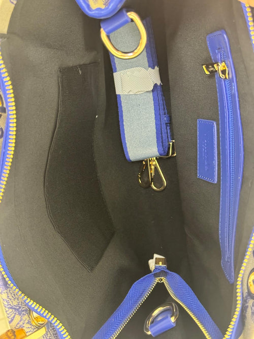 Innenfutter grau mit kleinem Fach links und rechts Fach mit Reißverschluss. Auf dem Boden ist der weiß-blaue Tragegurt der Tasche.