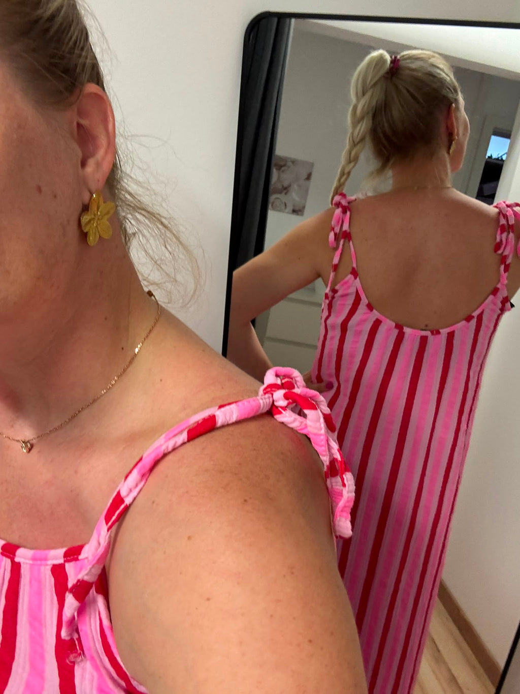 Kleid mit horizontalen Streifen ca. 3-4 cm Dick in pink, rosa und rot abwechselnd.
Der Saum ist dann vertikal in gleicher Farbe gestreift. Spaghettiträger mit knoten Rückansicht im Spiegel