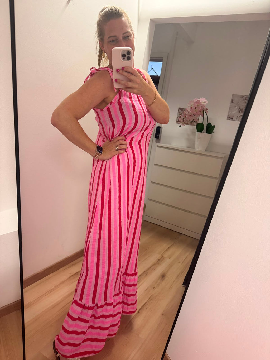 Kleid mit horizontalen Streifen ca. 3-4 cm Dick in pink, rosa und rot abwechselnd.
Der Saum ist dann vertikal in gleicher Farbe gestreift. Spaghettiträger mit knoten. Seitenansicht.