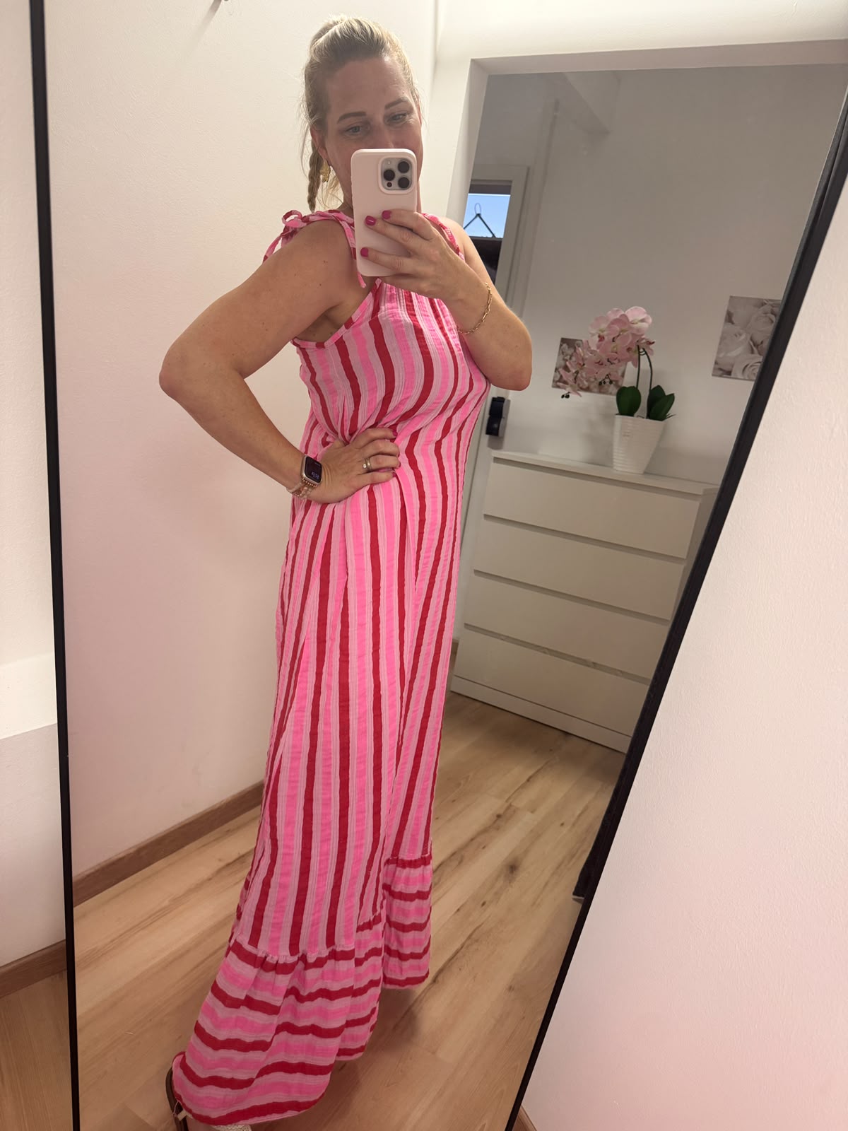 Kleid mit horizontalen Streifen ca. 3-4 cm Dick in pink, rosa und rot abwechselnd.
Der Saum ist dann vertikal in gleicher Farbe gestreift. Spaghettiträger mit knoten. Seitenansicht.